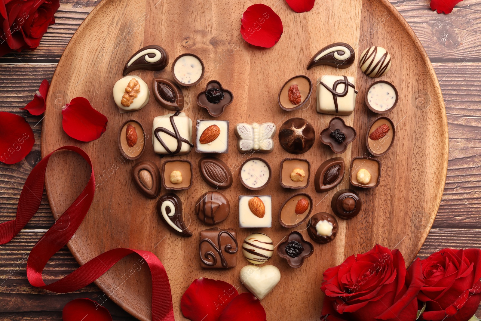 Photo of Heart made with delicious chocolate candies and rose petals on wooden table, top view