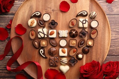 Heart made with delicious chocolate candies and rose petals on wooden table, top view