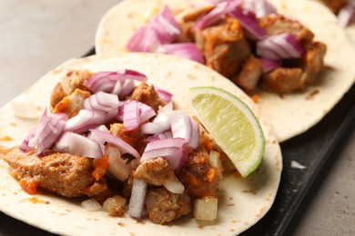 Delicious tacos with vegetables, meat and lime on grey table, closeup