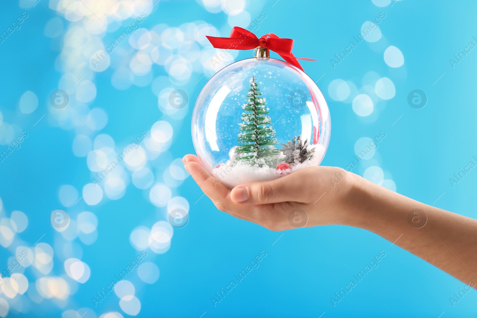 Photo of Woman holding decorative snow globe against blurred festive lights, closeup