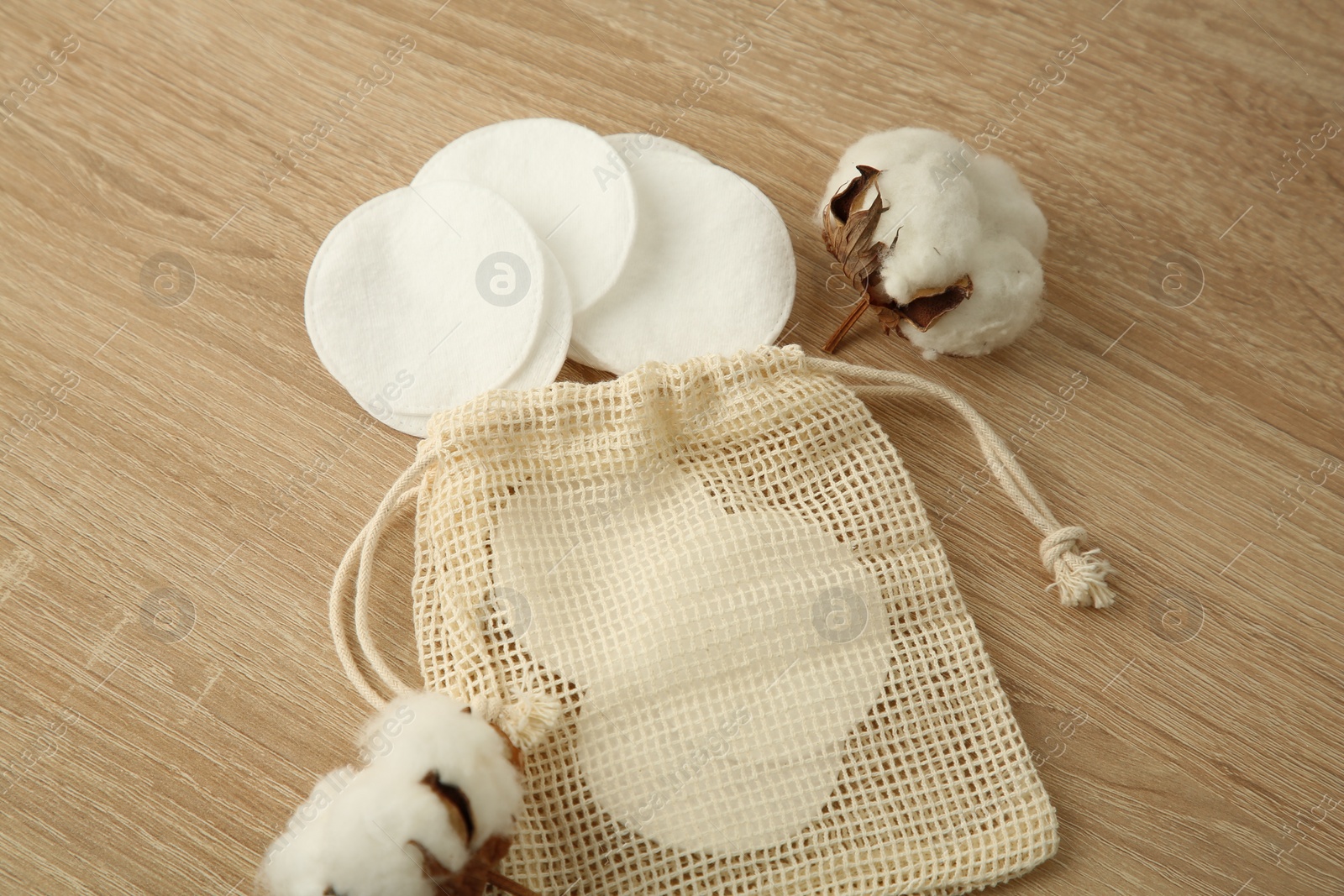 Photo of Cotton pads, bag and flowers on wooden table