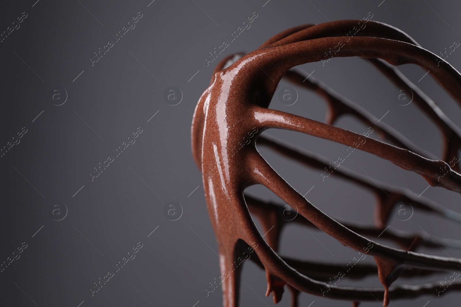 Photo of Chocolate cream flowing from whisk on grey background, closeup. Space for text