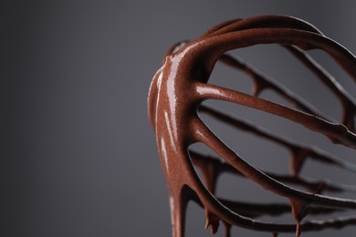 Chocolate cream flowing from whisk on grey background, closeup. Space for text
