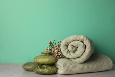 Photo of Composition with spa stones, towels and flowers on beige table against turquoise background. Space for text