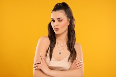 Beautiful woman with elegant jewelry blowing kiss on orange background