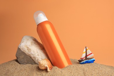 Photo of Sand with bottle of sunscreen, stone, seashell and ship figure against orange background. Sun protection