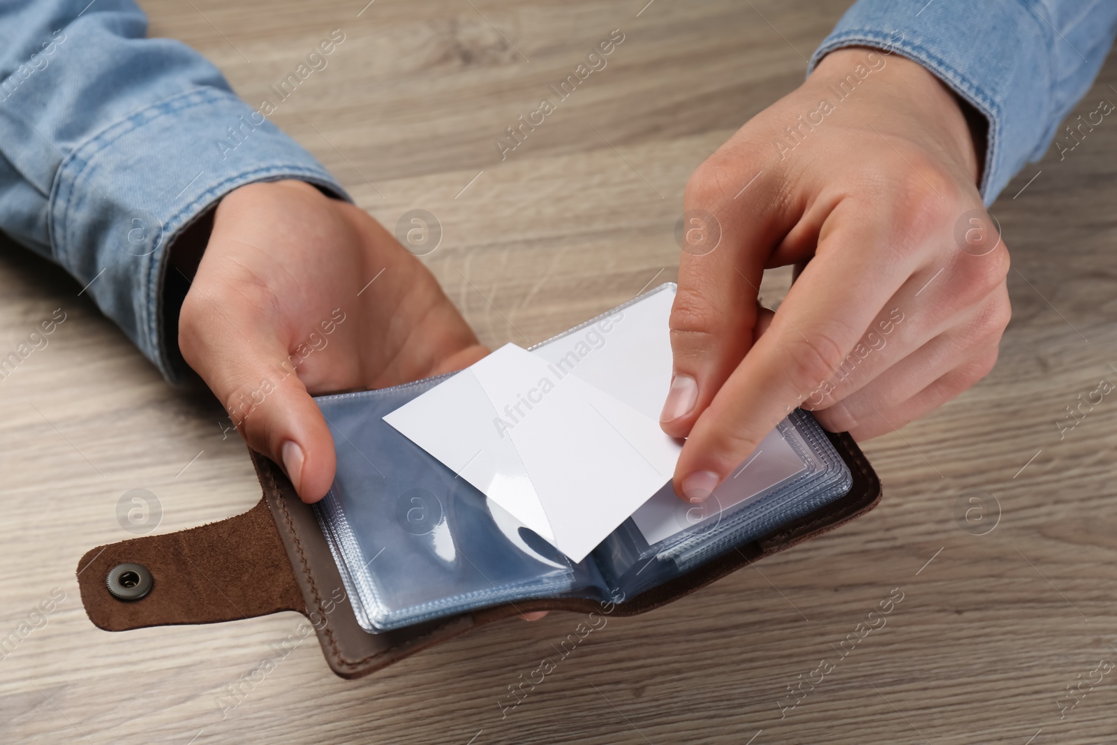 Photo of Man holding leather business card holder with blank card at wooden table, closeup