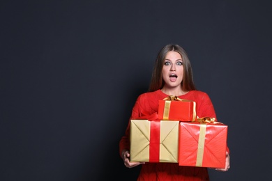 Photo of Emotional young woman with Christmas gifts on dark background. Space for text
