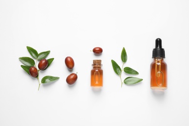 Glass bottles with jojoba oil and seeds on white background, top view