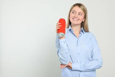 Beautiful happy woman holding red beverage can on light background. Space for text