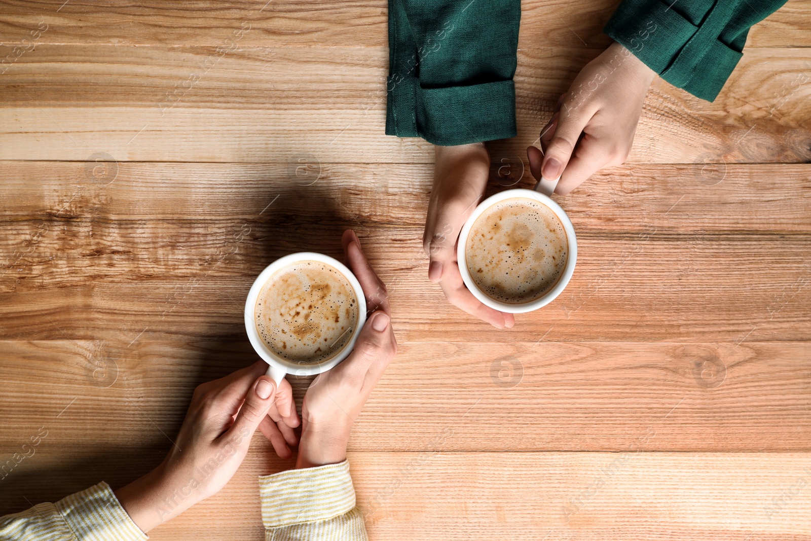 Photo of Women with cups of coffee at wooden table, top view