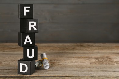Photo of Black cubes with word Fraud and money on wooden table, space for text