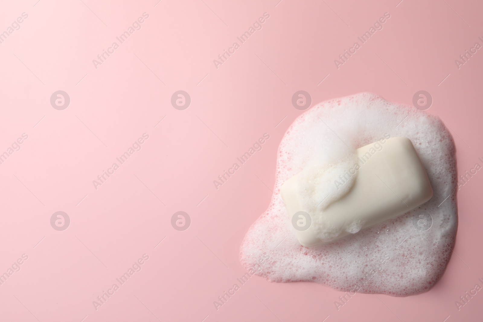 Photo of Soap with fluffy foam on pink background, top view. Space for text