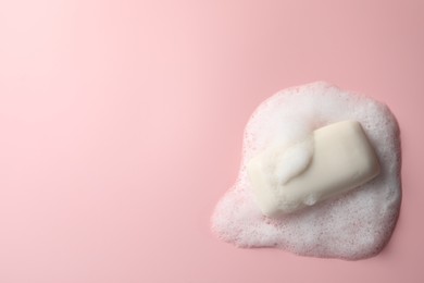 Soap with fluffy foam on pink background, top view. Space for text