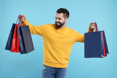 Photo of Smiling man with many paper shopping bags on light blue background