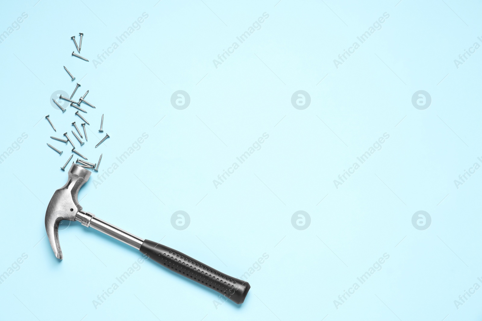 Photo of Hammer and metal nails on light blue background, flat lay. Space for text