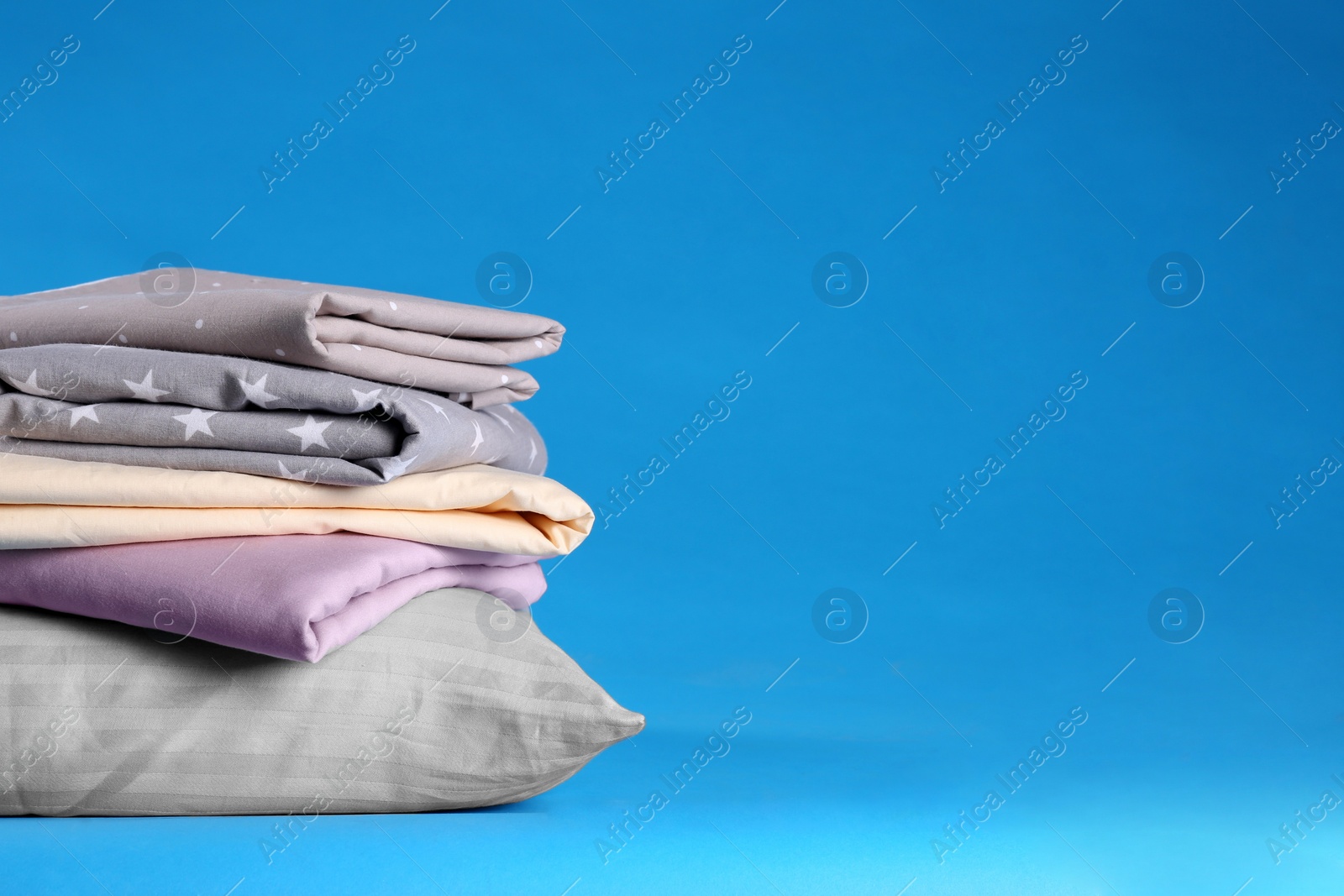 Photo of Stack of clean bed sheets and pillow on blue background. Space for text