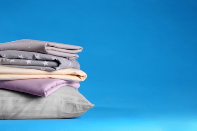 Stack of clean bed sheets and pillow on blue background. Space for text