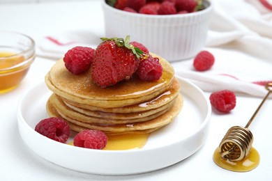 Tasty pancakes with fresh berries and honey on white table