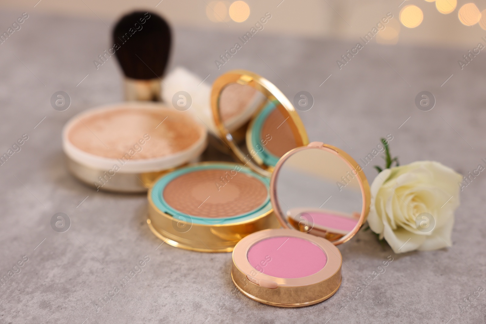 Photo of Composition with bronzer, blusher and rose flower on grey textured table, closeup