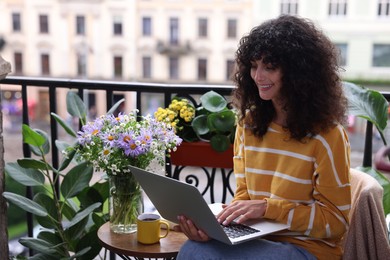 Beautiful young woman using laptop on balcony with green houseplants