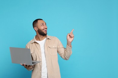 Smiling young man with laptop on light blue background, space for text