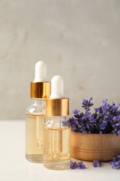 Photo of Bottles of essential oil and lavender flowers on white wooden table