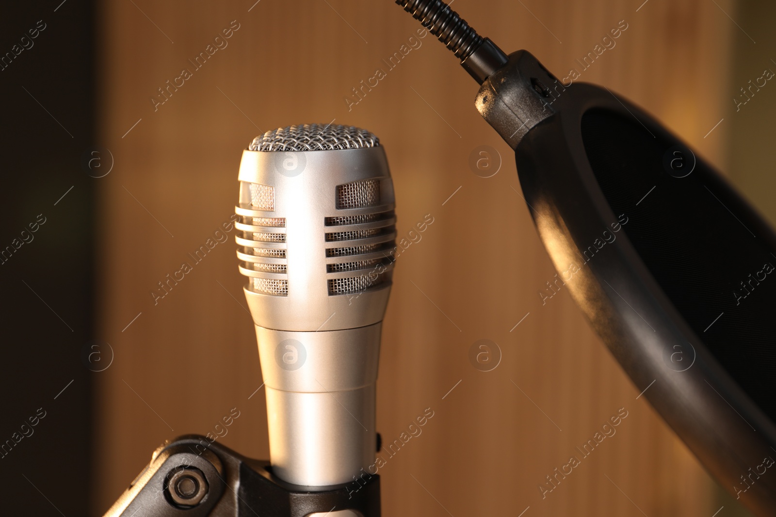 Photo of Stand with microphone and pop filter on blurred background, closeup. Sound recording and reinforcement