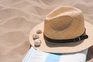 Photo of Straw hat with seashells and beach towel on sand, space for text