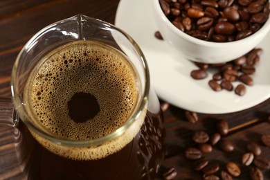 Photo of Glass turkish coffee pot with hot drink and beans on wooden table, above view