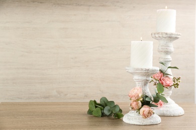 Photo of White candlesticks with burning candles and floral decor on wooden table. Space for text