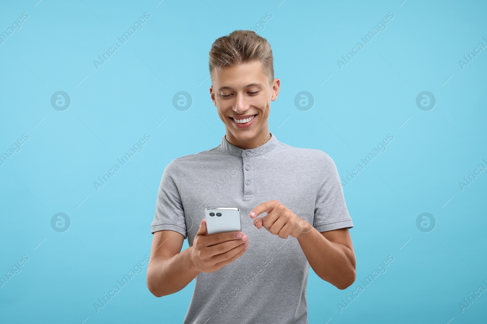 Photo of Happy young man sending message via smartphone on light blue background