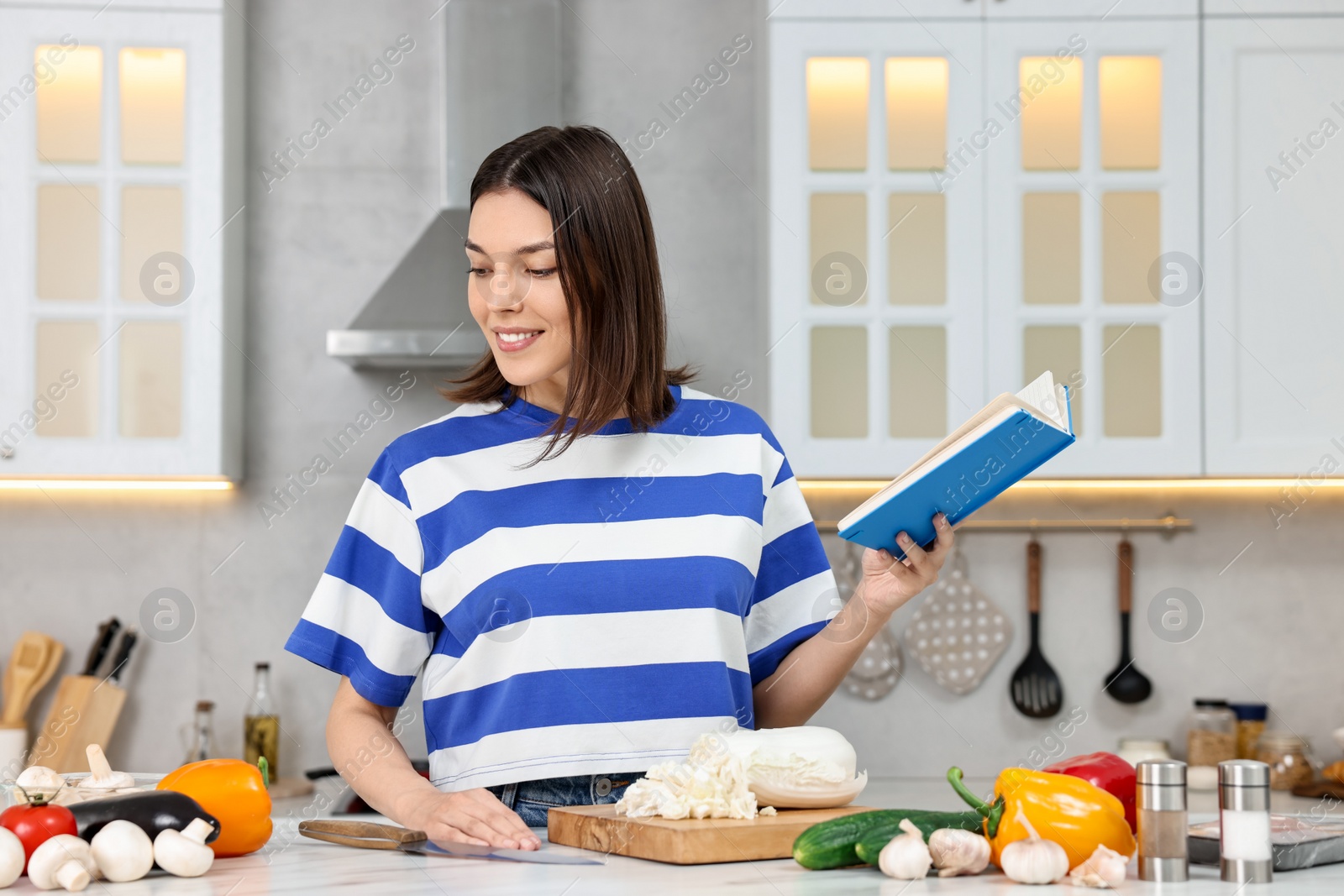 Photo of Happy woman with recipe book at table in kitchen