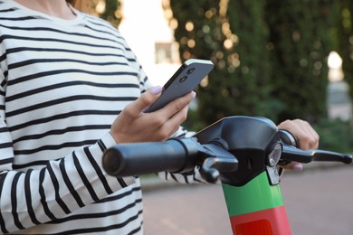 Woman using smartphone to pay and unblock electric kick scooter outdoors, closeup