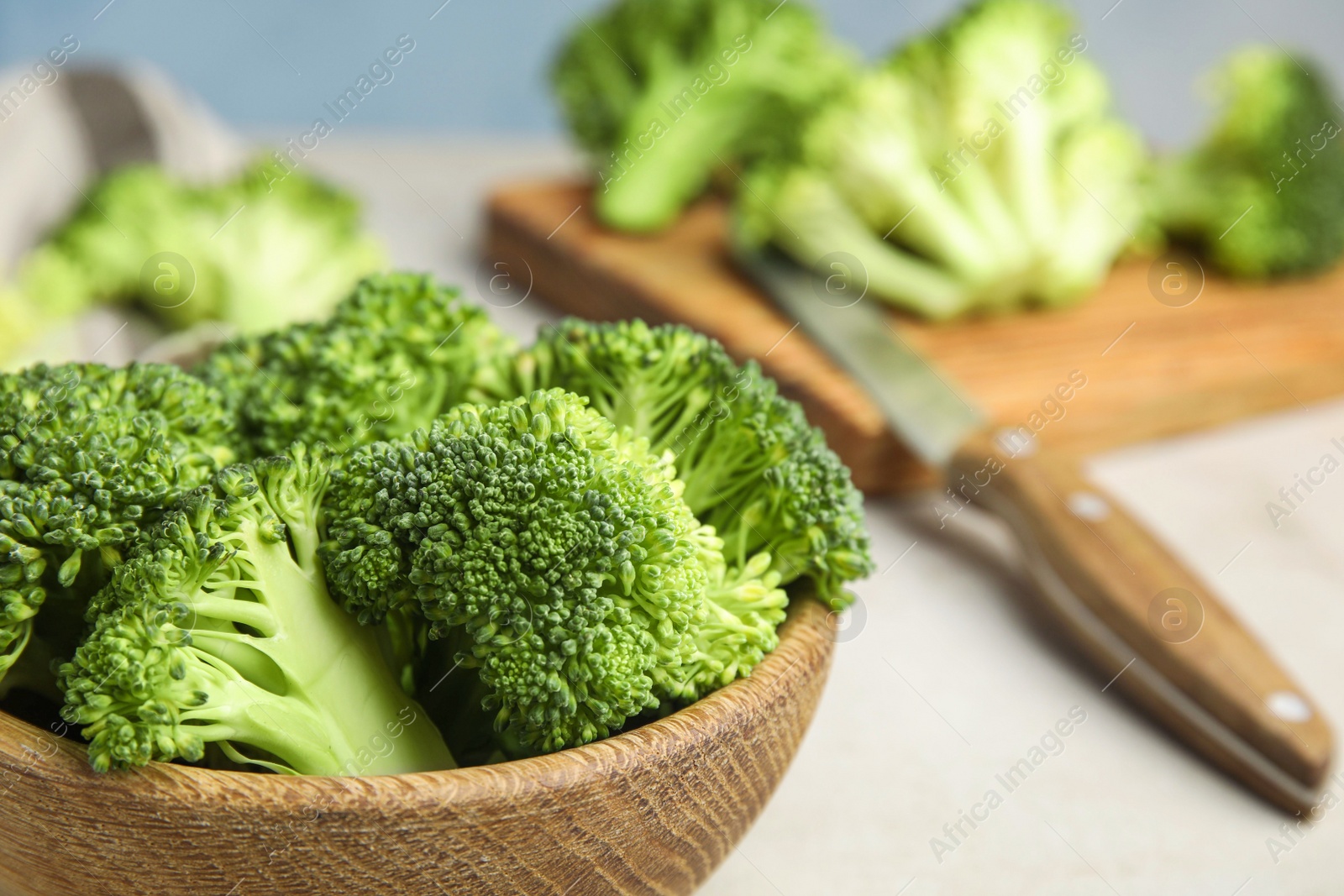 Photo of Fresh green broccoli in wooden bowl on light table, closeup