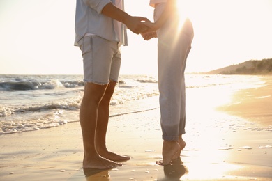 Photo of Couple on sandy beach near sea at sunset, closeup of legs