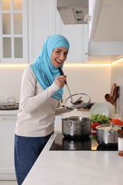 Photo of Muslim woman cooking dish in saucepan on cooktop indoors