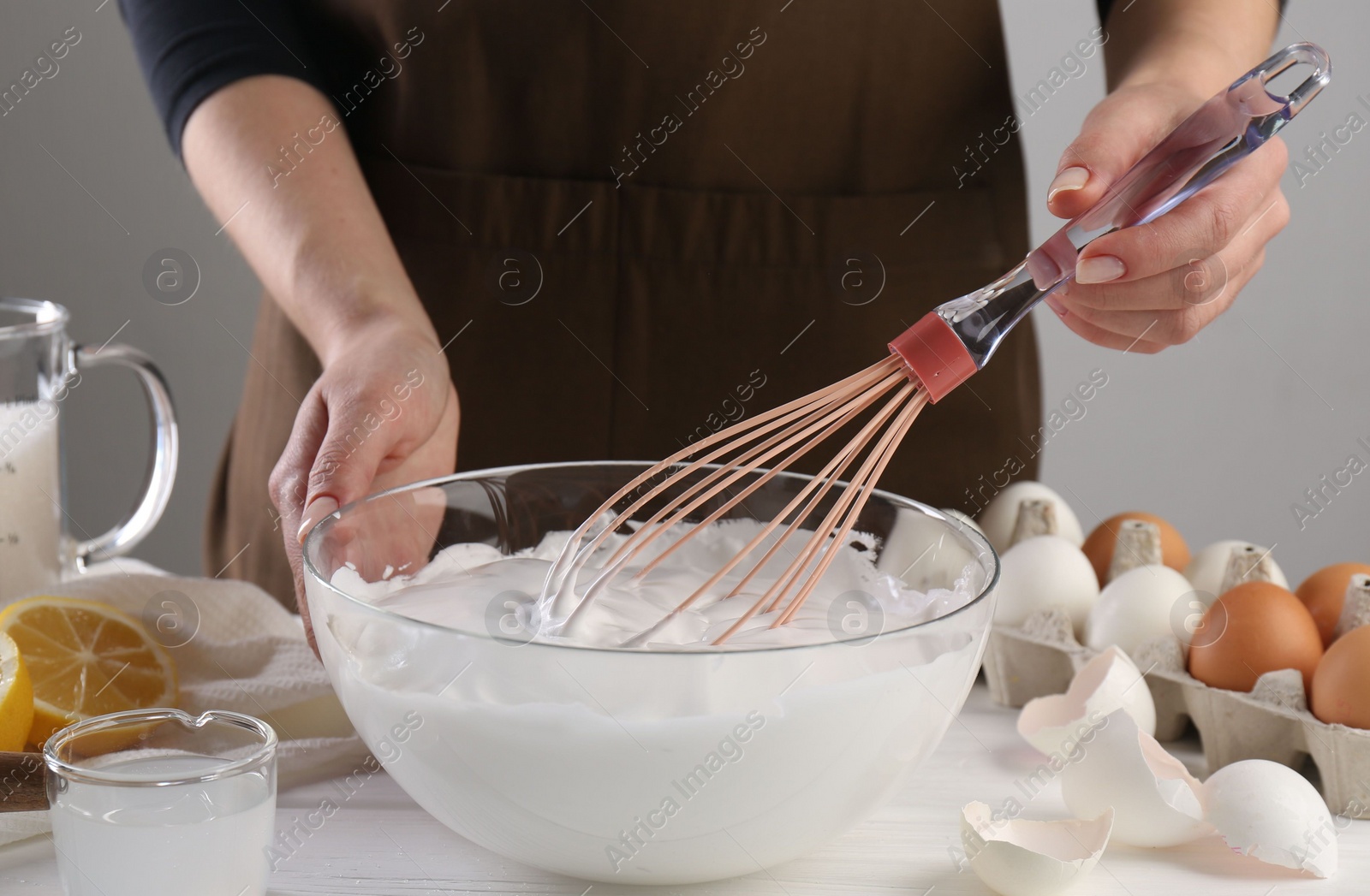 Photo of Woman making whipped cream with whisk at white wooden table, closeup