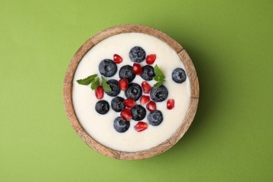 Photo of Bowl of delicious semolina pudding with blueberries, pomegranate and mint on green background, top view