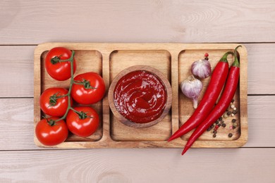 Plate with delicious ketchup in bowl, peppercorns and products on light wooden table, top view. Tomato sauce