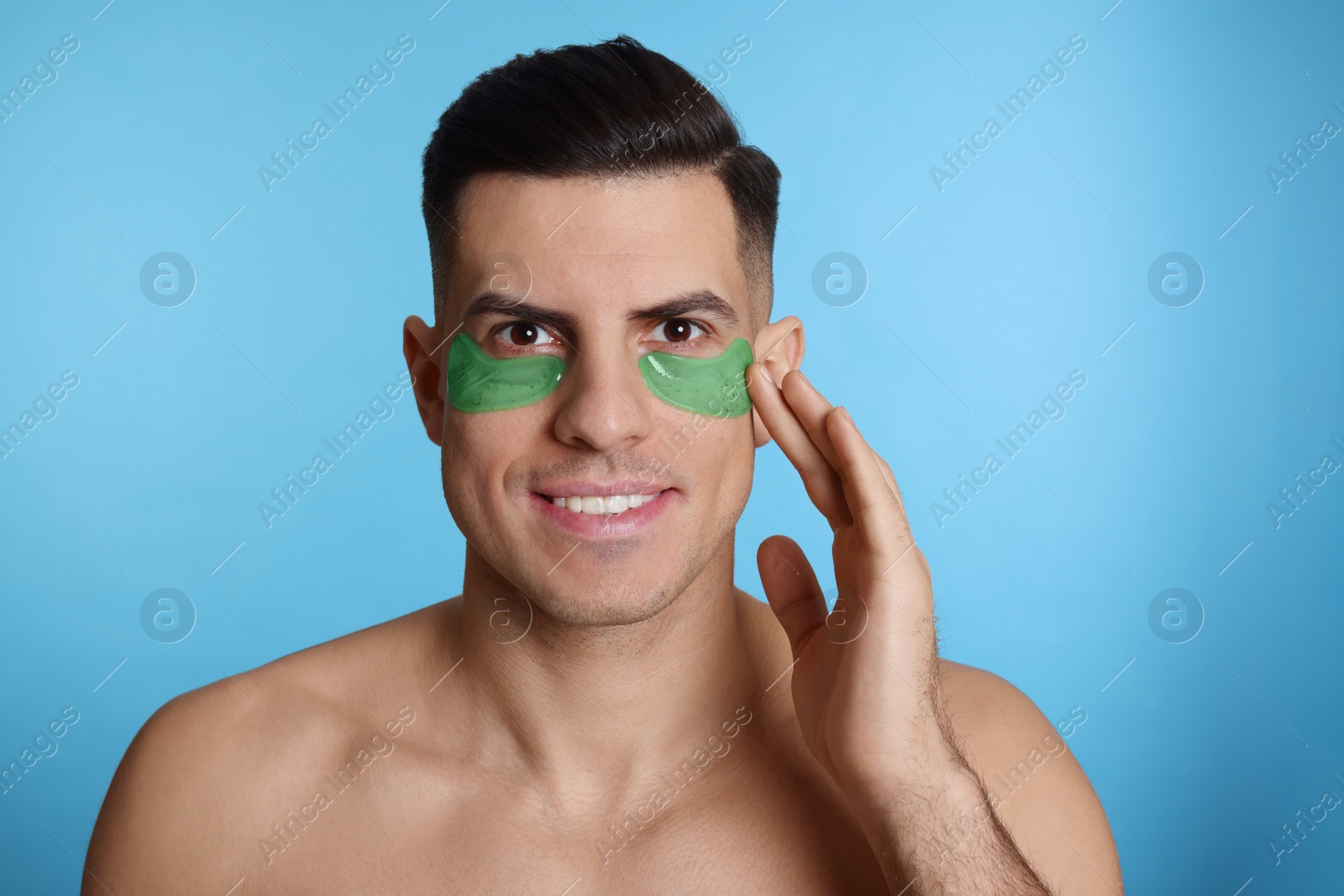 Photo of Man applying green under eye patch on light blue background