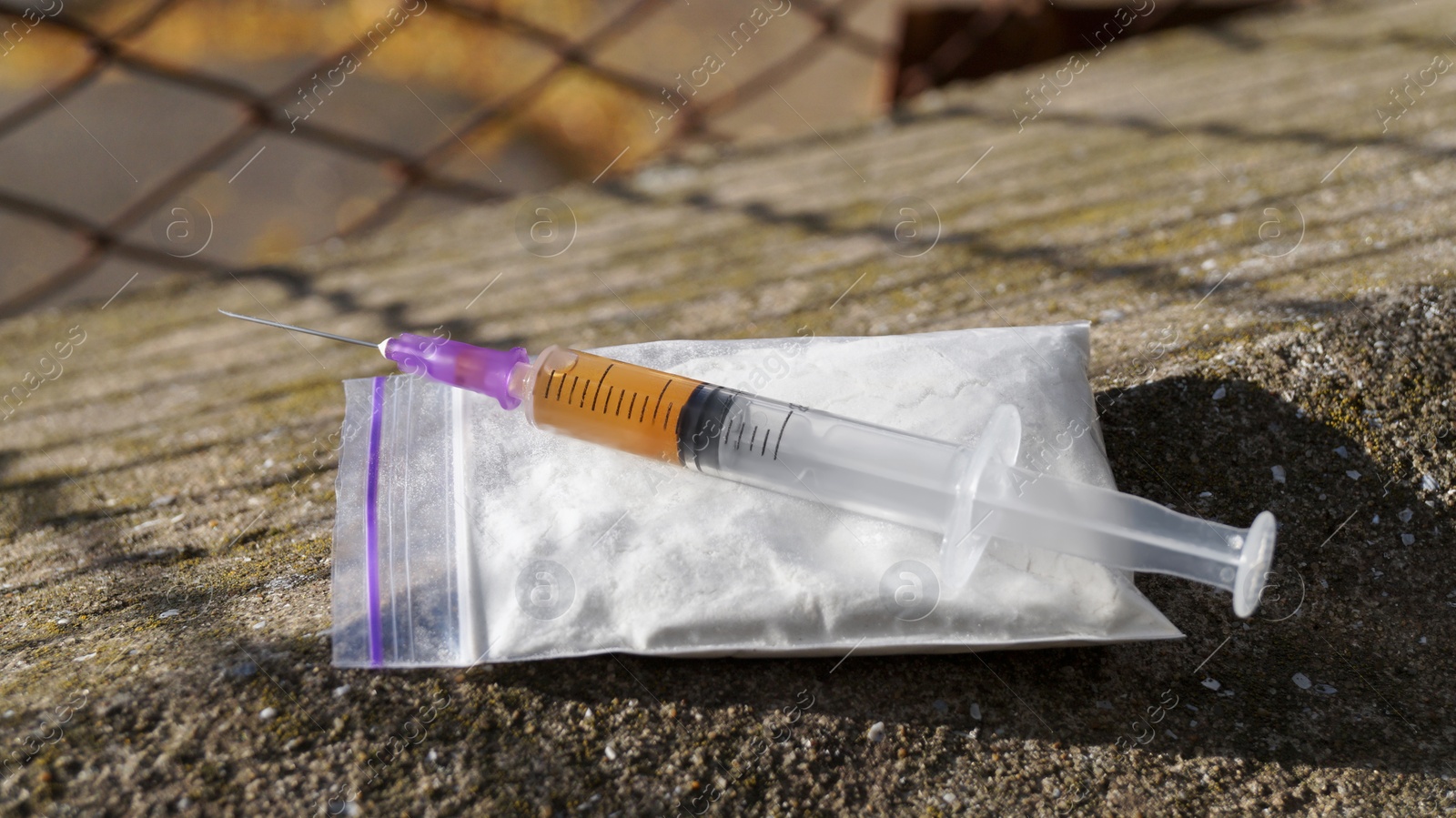 Photo of Plastic bag with powder and syringe on stone surface outdoors, closeup. Hard drugs