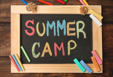 Photo of Little blackboard with text SUMMER CAMP chalked in different colors on table, top view