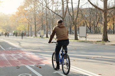 Photo of Man riding bicycle on lane in city, back view