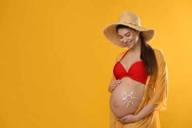 Photo of Young pregnant woman with sun protection cream on belly against yellow background, space for text