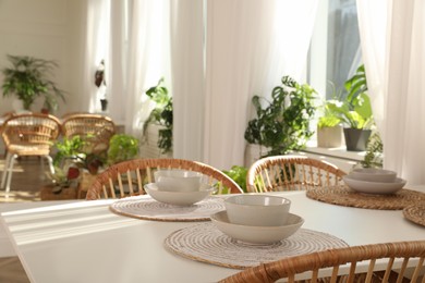 Photo of Stylish dining table and wicker chairs near window in room. Interior design