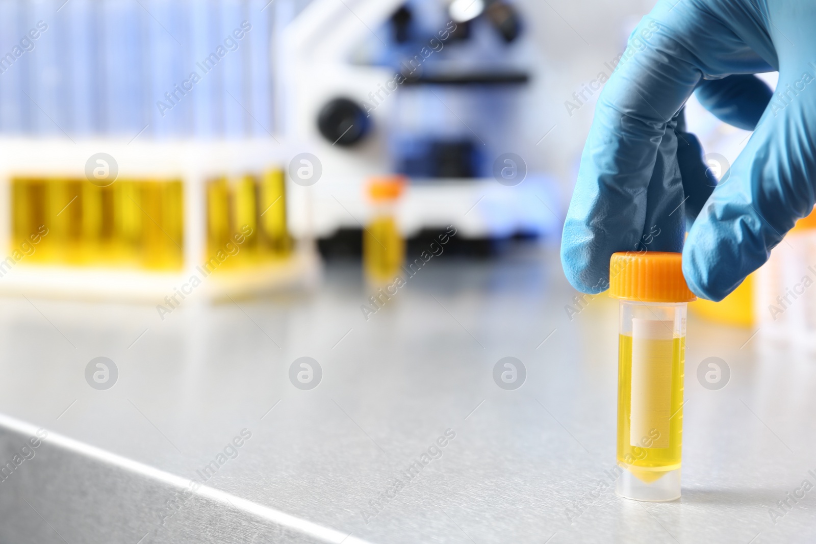 Photo of Laboratory assistant holding urine sample in container at table, closeup with space for text. Medical analysis