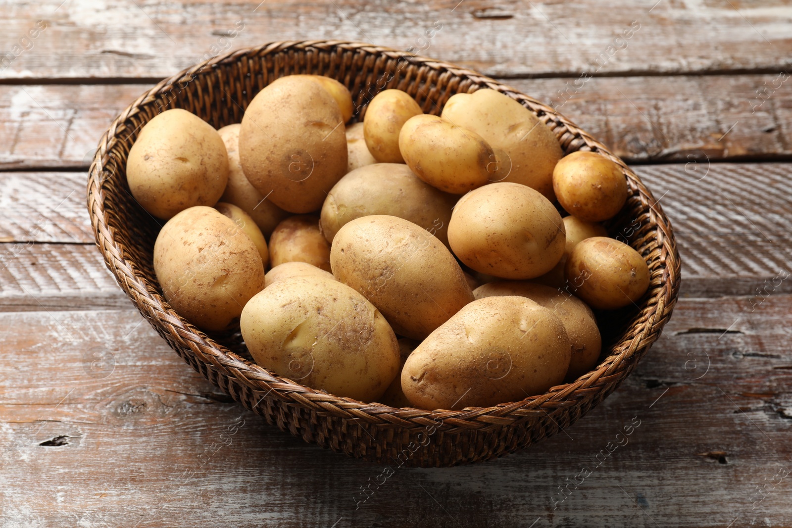 Photo of Raw fresh potatoes in wicker basket on wooden table