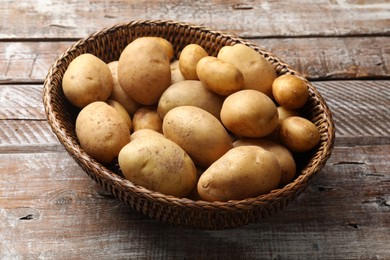 Photo of Raw fresh potatoes in wicker basket on wooden table