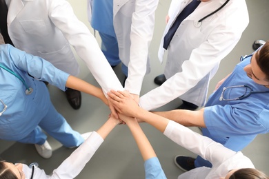 Photo of Team of medical workers holding hands together indoors, top view. Unity concept